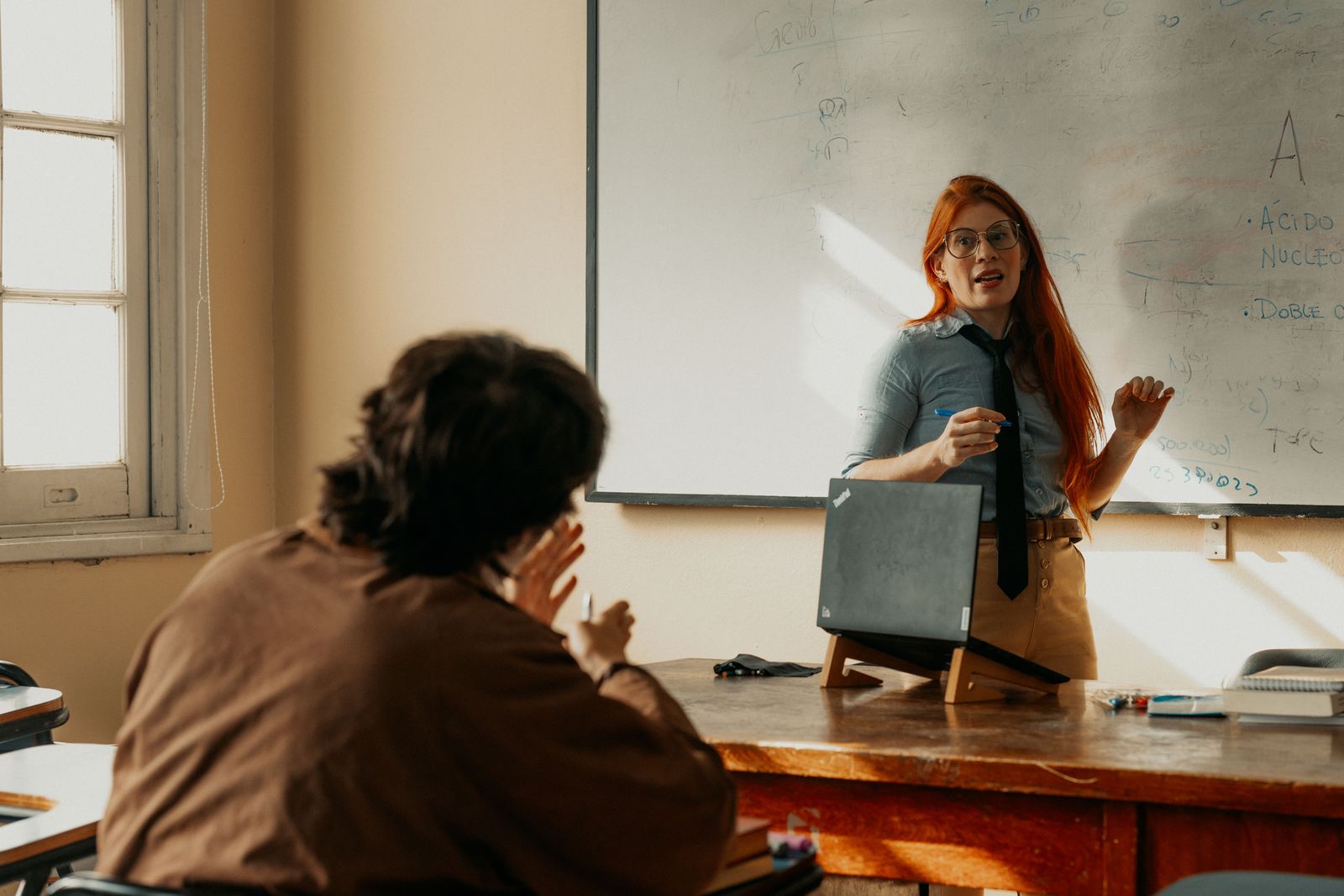 Una docente conversa con un estudiante frente a la pizarra